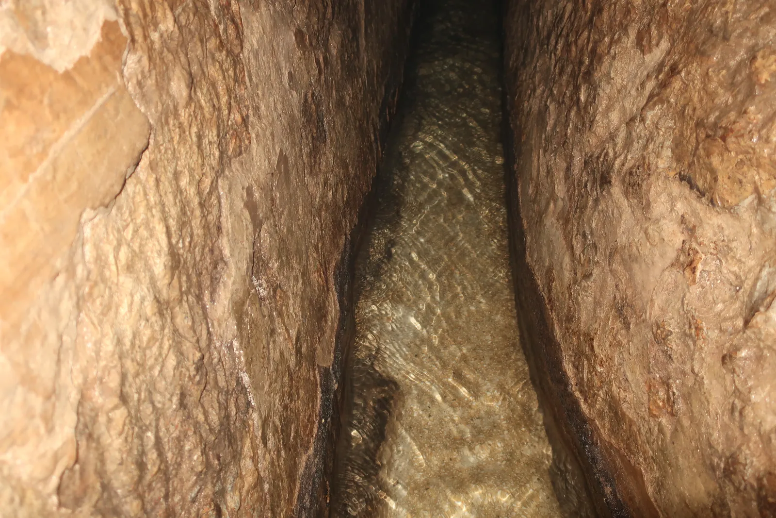 Uski tunel isklesan u stijeni, s vodom na dnu